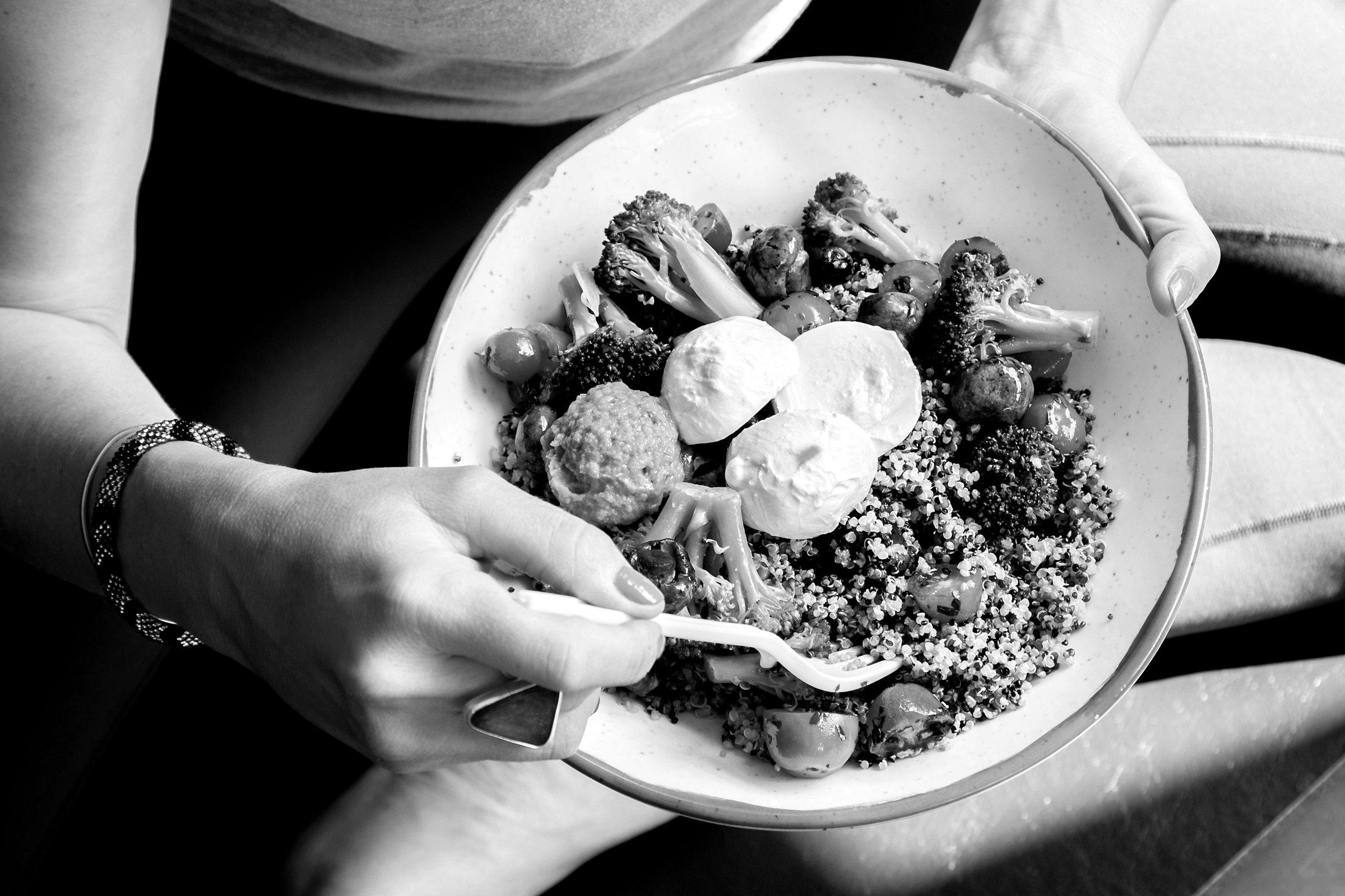A bowl of quinoa, roasted vegetables and mozzarella, held on someone's lap