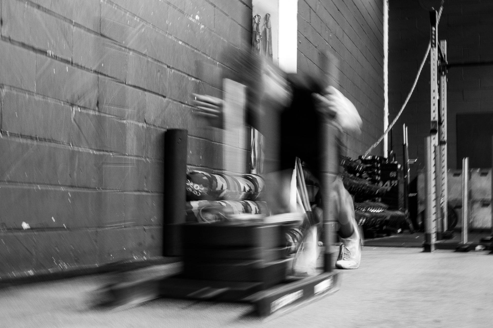 Someone driving a loaded sled along a gym wall, blurred with speed