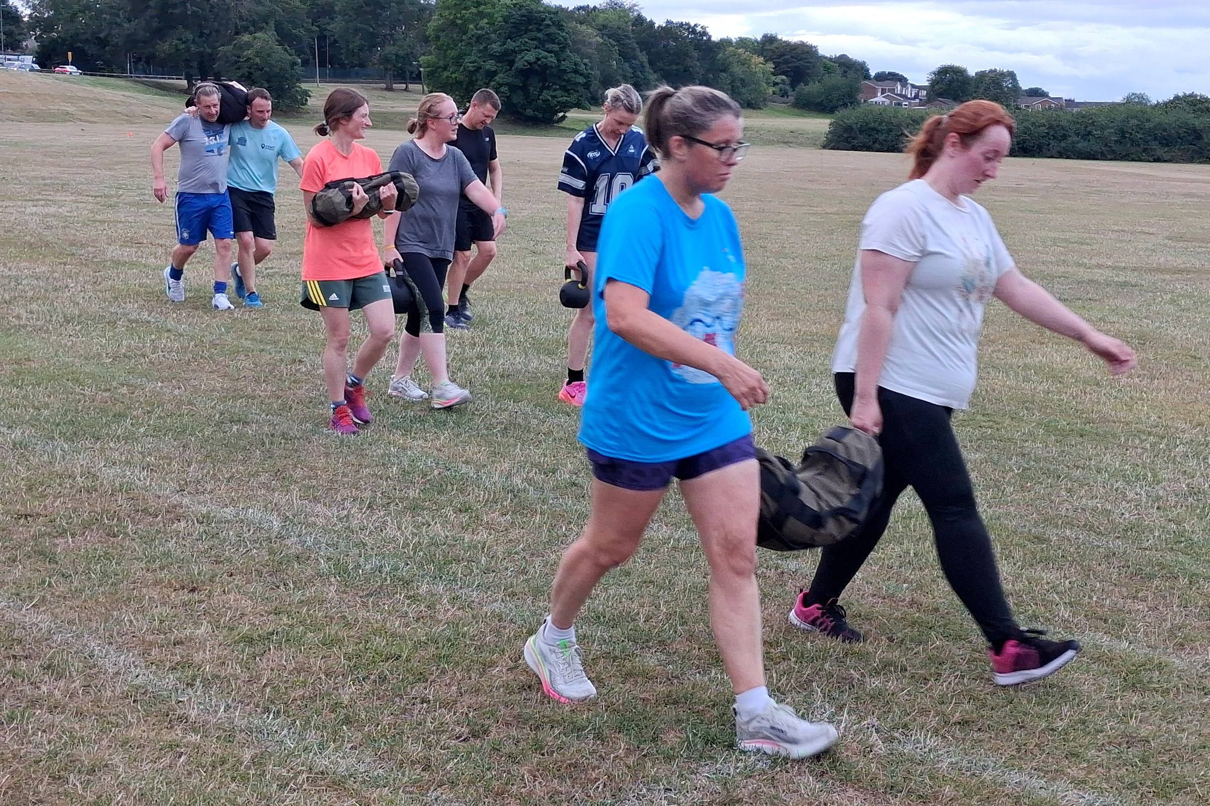 A CommFit group carrying sandbags and kettlebells across a field in Whickham
